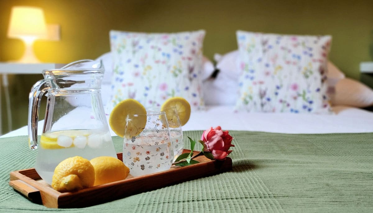 Apartamento Granate 4. Detalle de la cama doble con una bandeja en primer plano con bebidas, limones y flores